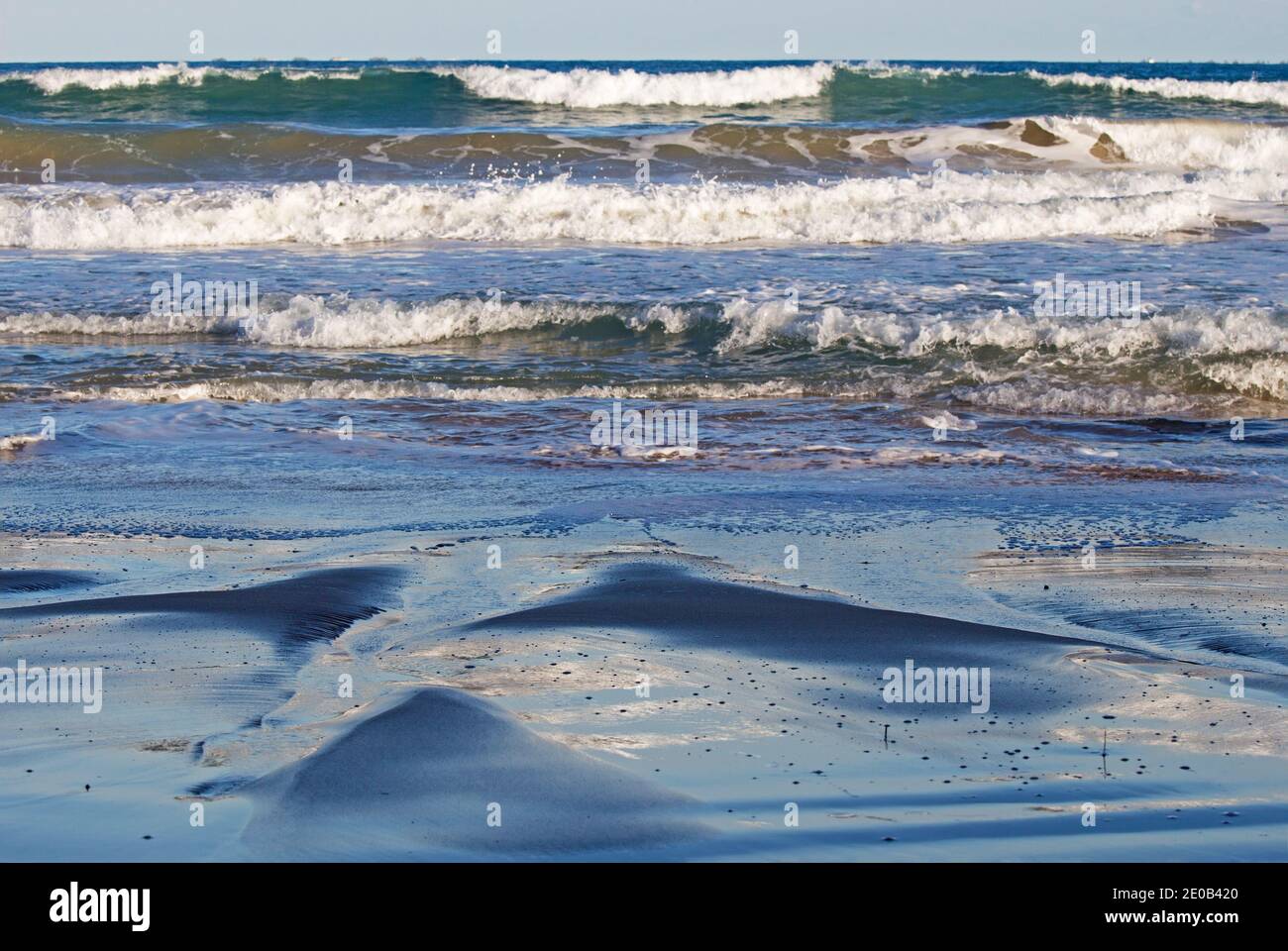 The sea can create some rather interesting effects - flowing onto the sand beach and dispersing over the channels formed. Stock Photo