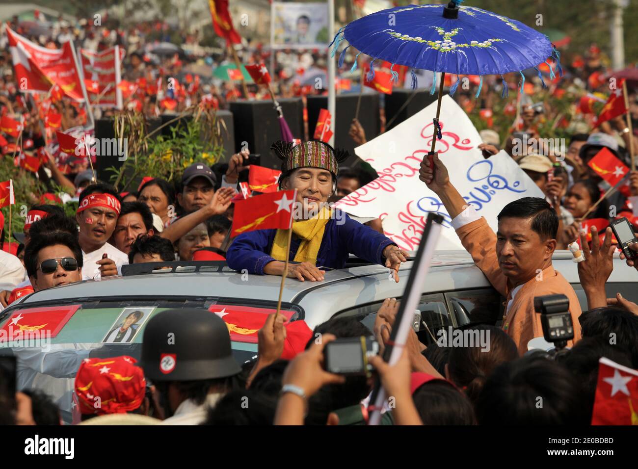 Nobel Peace Prize winner and National League for Democracy (NLD) chairman Aung San Suu Kyi, wearing a traditional Shan costume, reaches to touch the hands of her supporters, as her private photographer (holding an umbrella), who is also one of her bodyguards stares at a man wearing a German army helmet with a nazi swastika, during a campaign meeting in Lashio, northern Shan State, Myanmar on March 17, 2012. Aung San suu Kyi refuses any particular security measures. Any assassination attempt would be easy. Photo by Christophe Loviny/ABACAPRESS.COM Stock Photo
