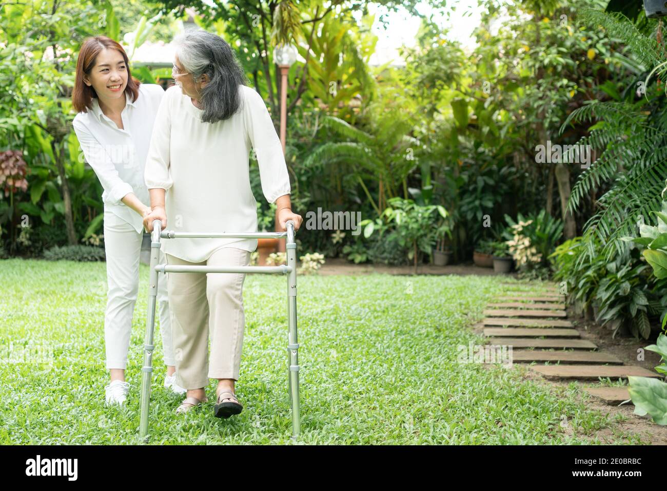 An old elderly Asian woman uses a walker and walking in the backyard with her daughter.  Concept of happy retirement With care from a caregiver and Sa Stock Photo