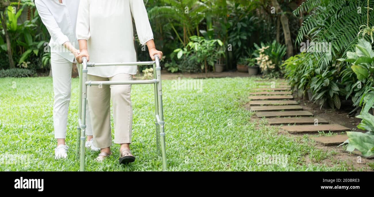 An old elderly Asian woman uses a walker and walking in the backyard with her daughter.  Concept of happy retirement With care from a caregiver and Sa Stock Photo