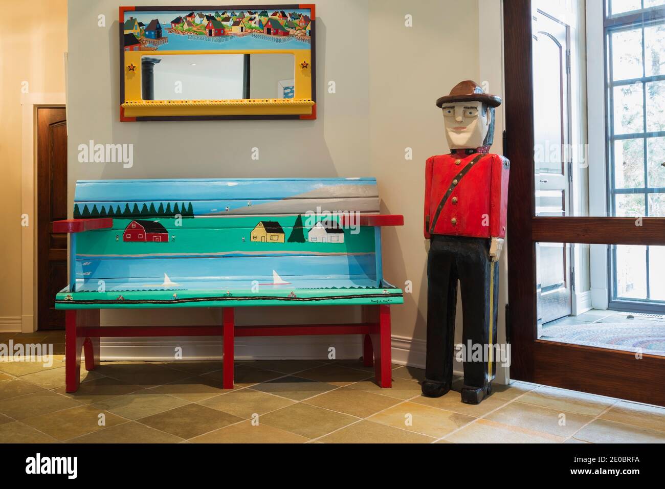 Canadian Mountie and blue, green and red painted folk art sitting bench next to entryway inside contemporary home Stock Photo