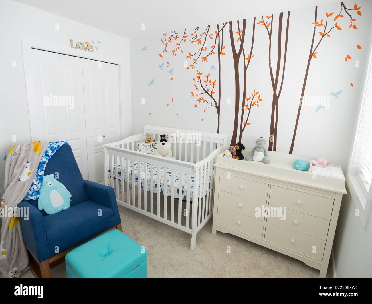 A decorated modern baby nursery bedroom with a crib, dresser, diaper change table, rocking chair, and no people. Stock Photo