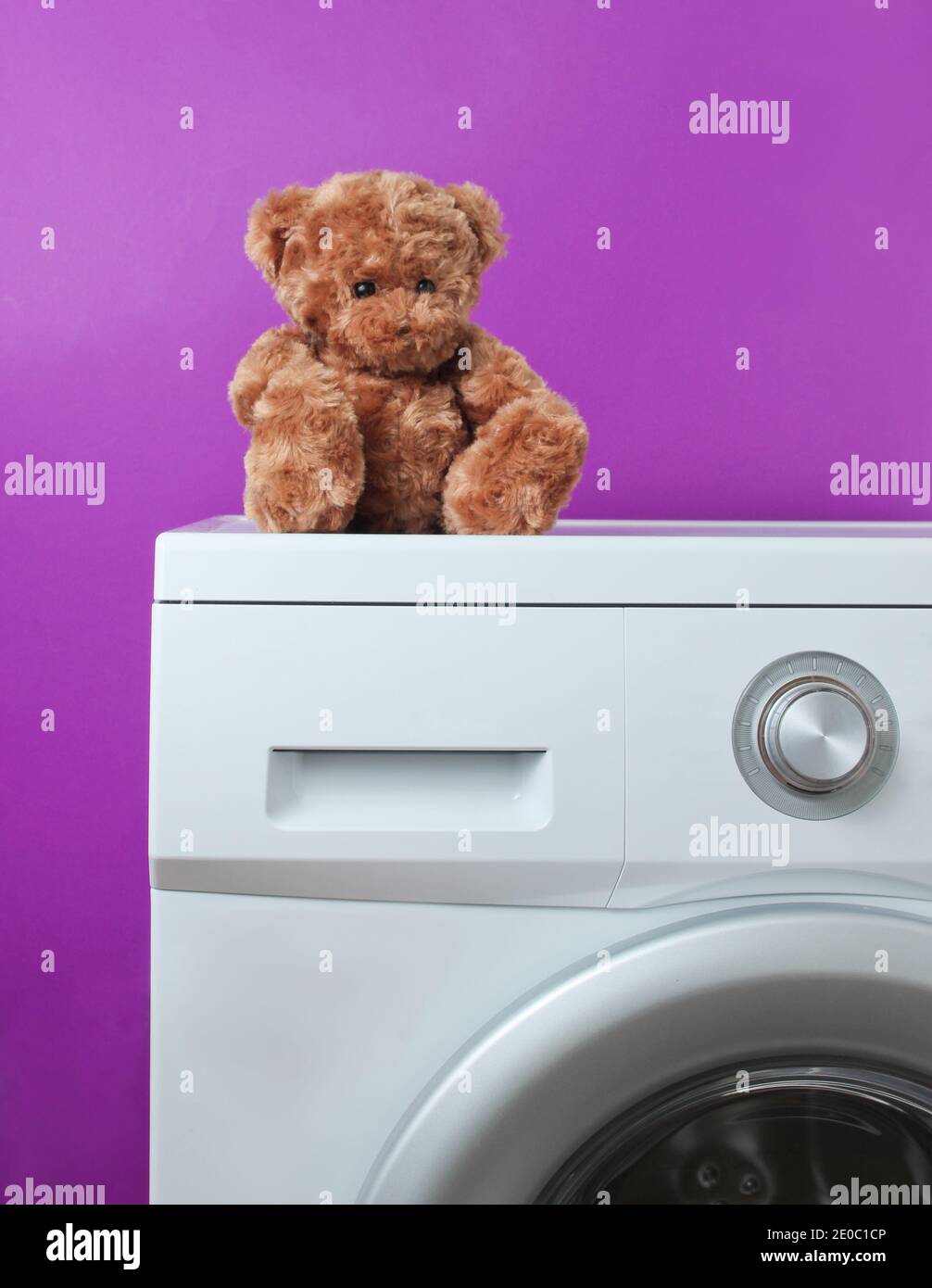 Teddy bear on a washing machine against purple background Stock Photo