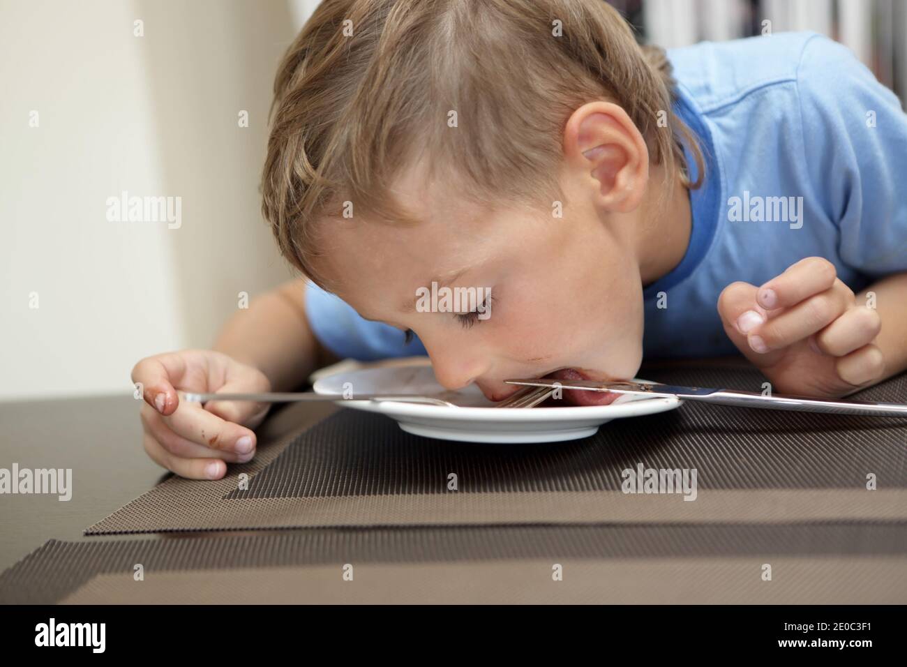 Child licking remnants of food from plate in cafe Stock Photo