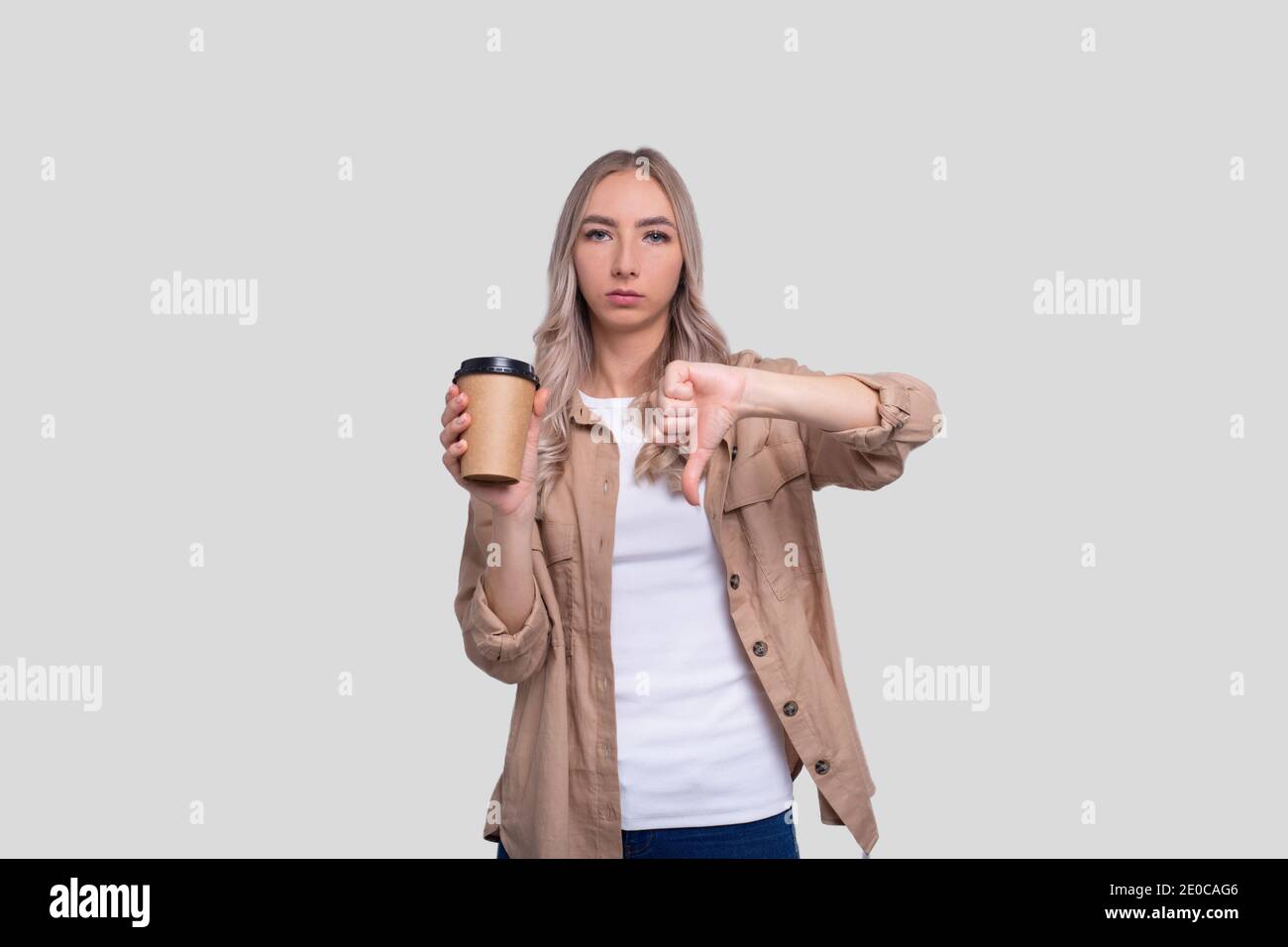 Girl Holding Take Away Coffee Cup Showing Thumb Down. Girl With To Go Coffee Cup in Hands. Stock Photo