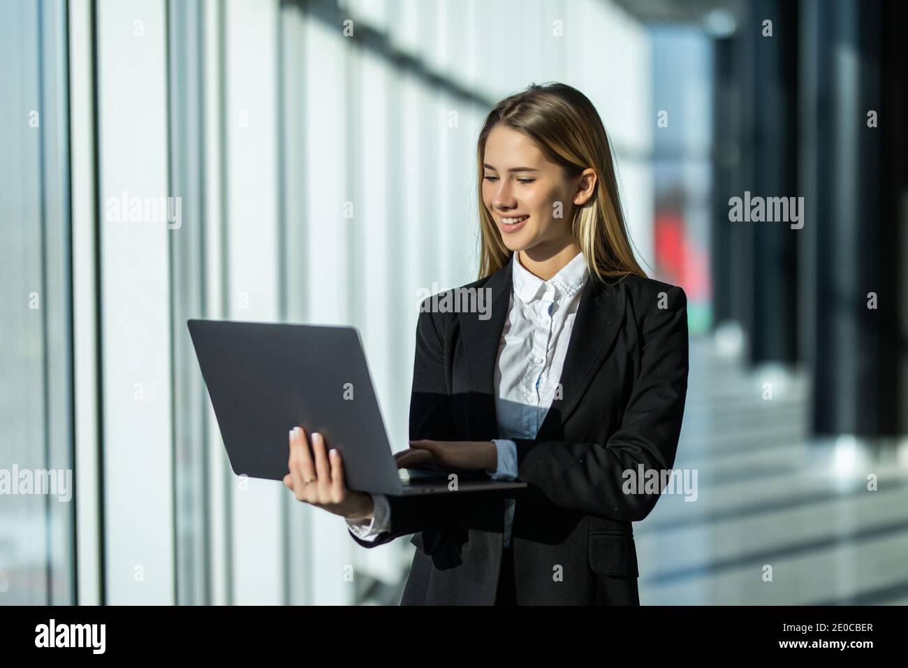 Young business woman with laptop standing in an office Stock Photo - Alamy
