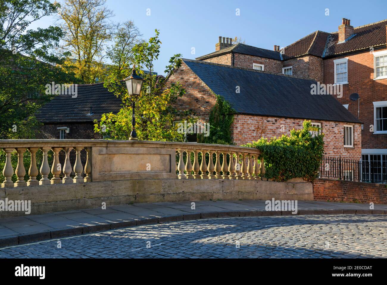 Foss Bridge & scenic cobbled street in York city - (historic Georgian stone balusters, sunlit setts on road, blue sky) - North Yorkshire, England, UK. Stock Photo