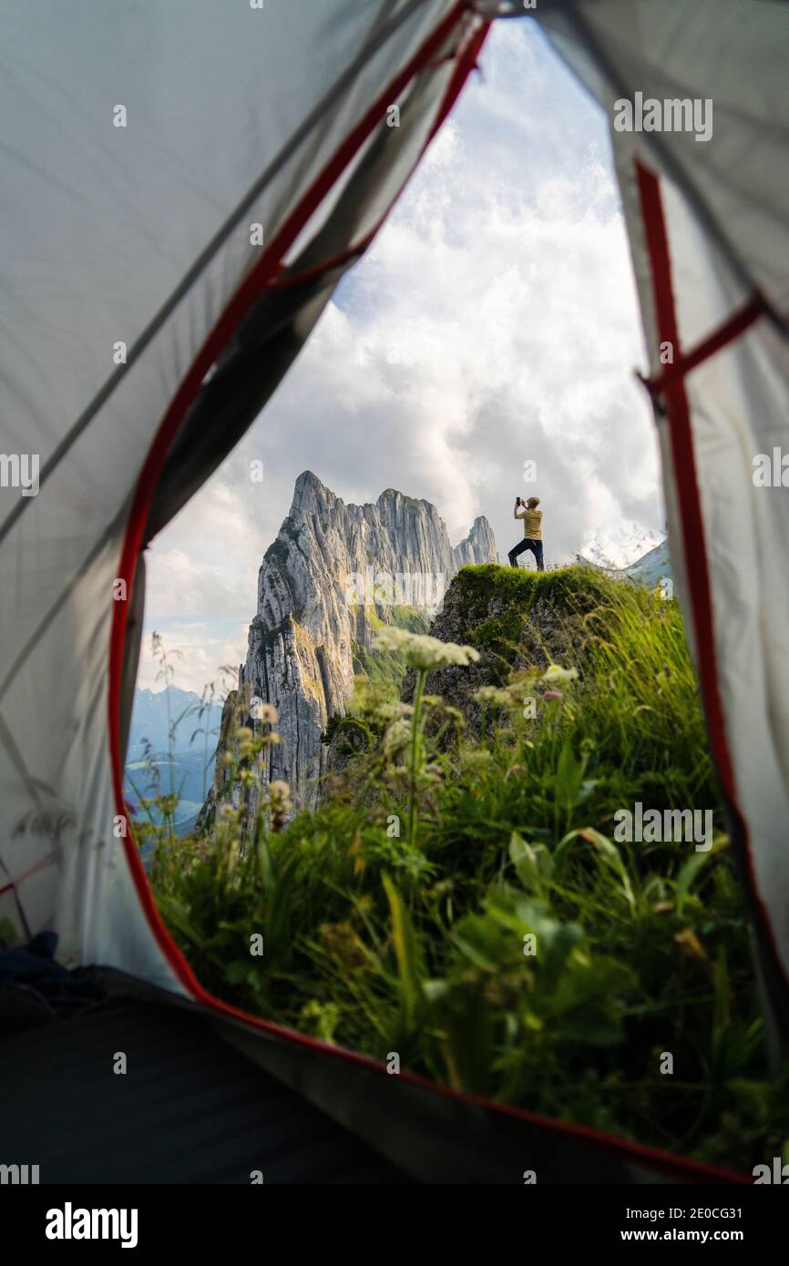 Man on rocks photographing Saxer Lucke mountain with smartphone seen from hiking tent, Appenzell Canton, Switzerland, Europe Stock Photo