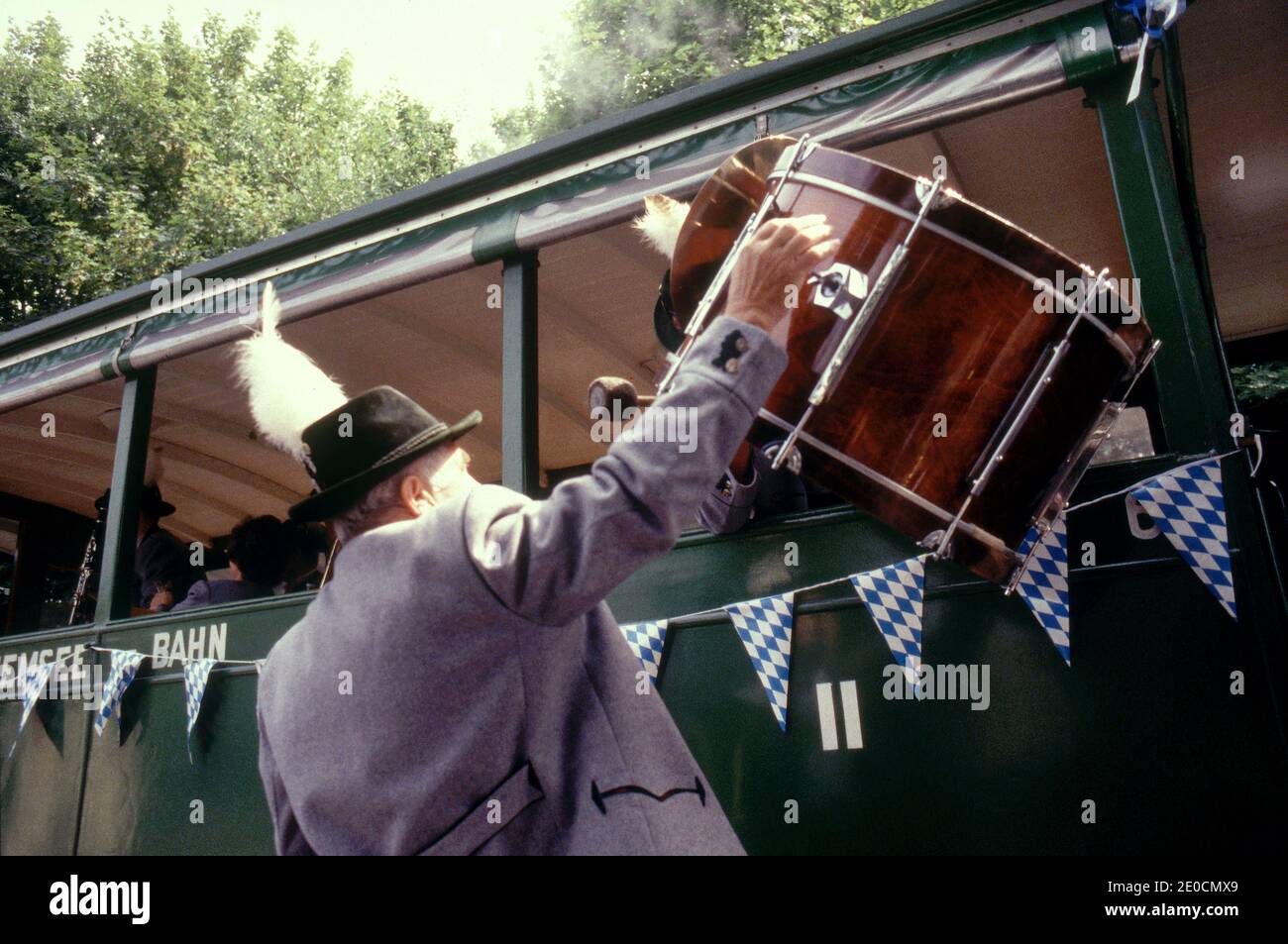 Germany/Bavaria/ Chiemsee/Man in traditional clothes traveling in a Train and his friend is helping to load his big Drum trough the Train window. Stock Photo
