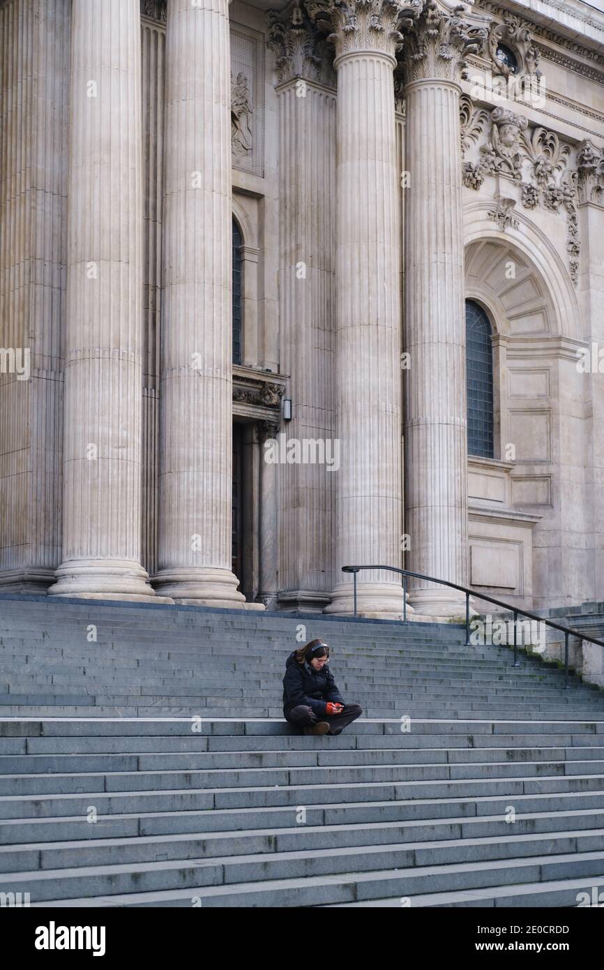 London, UK - December 2020 :  single woman sits on the steps pf St Pauls Cathedral, City of London Stock Photo