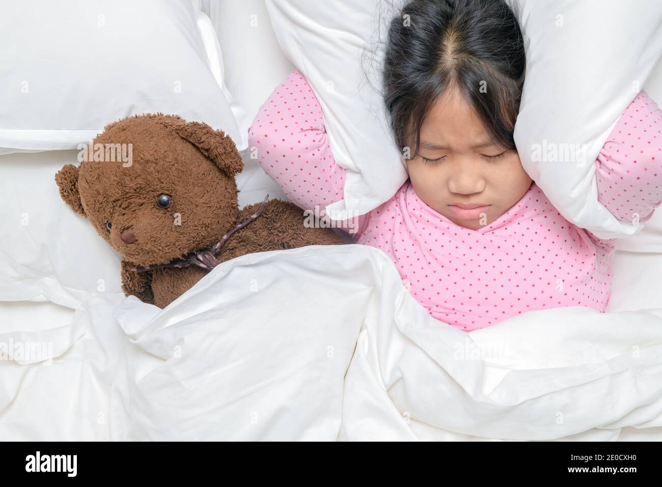 Little girl trying to sleep covering ears to avoid neighbor noise at