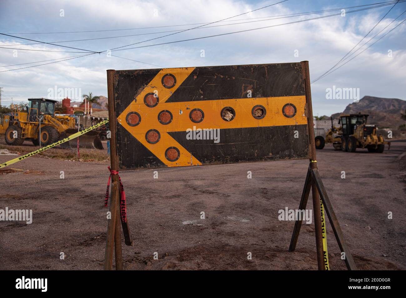 Closeup of warning sign with large orange arrow with reflectors, yellow construction equipment in soft focus in background, San Carlos, Sonora, Mx. Stock Photo