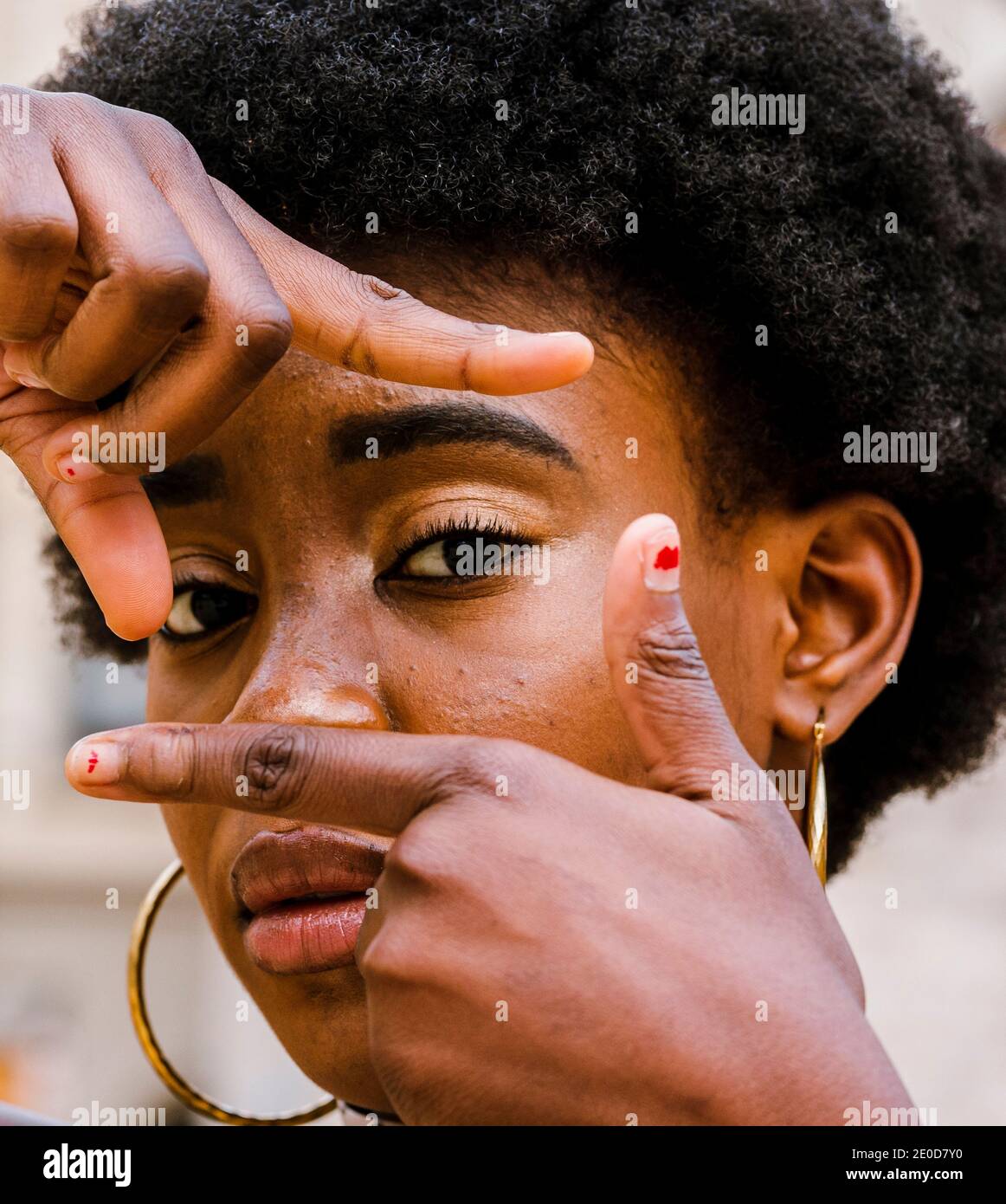 Serious young curly haired African American female making frame with fingers and looking at camera Stock Photo