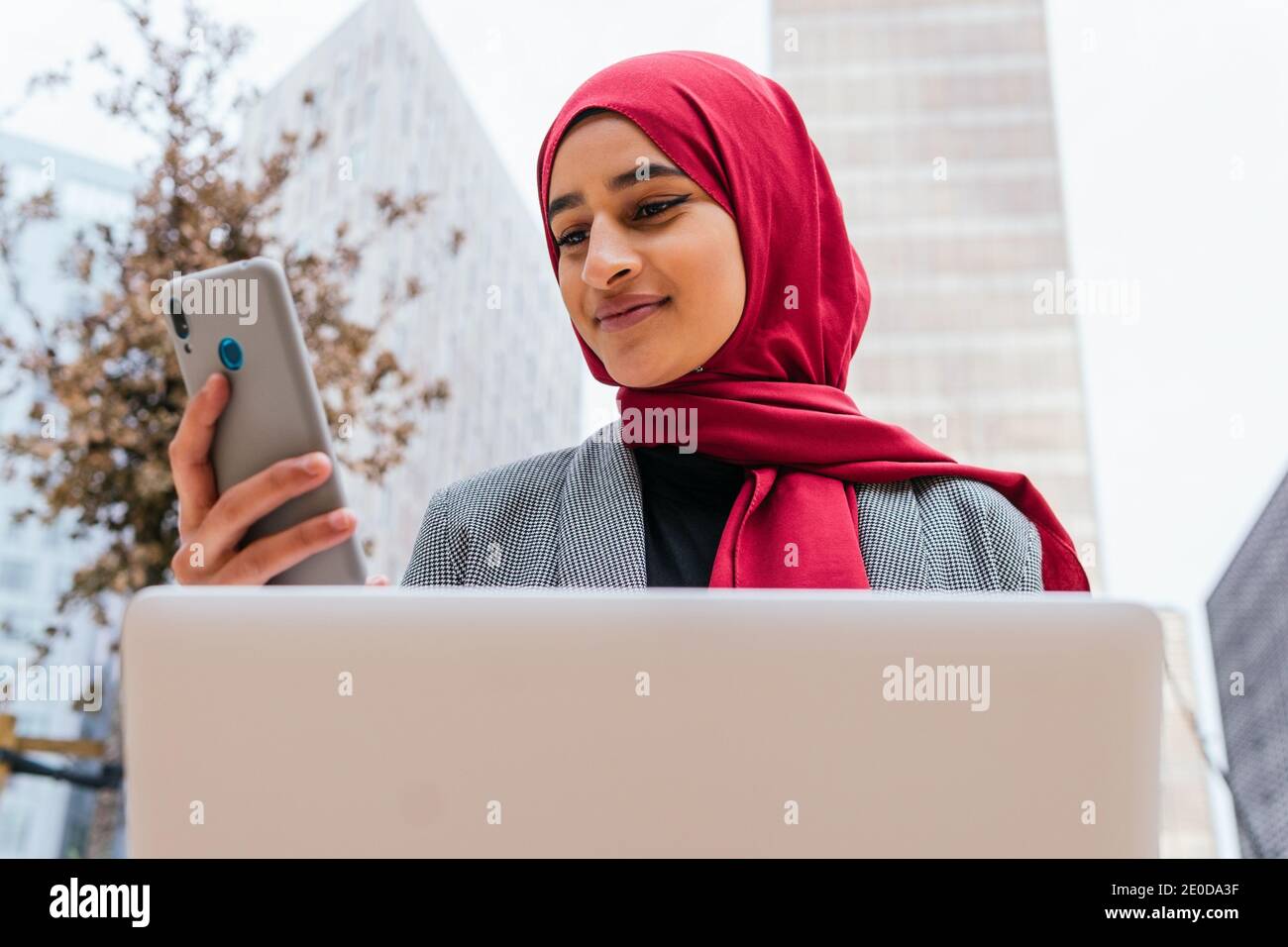 Cheerful Arab female freelancer in red hijab sitting with laptop on ...