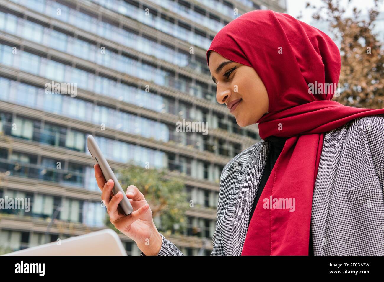 Cheerful Arab female freelancer in red hijab sitting with laptop on ...
