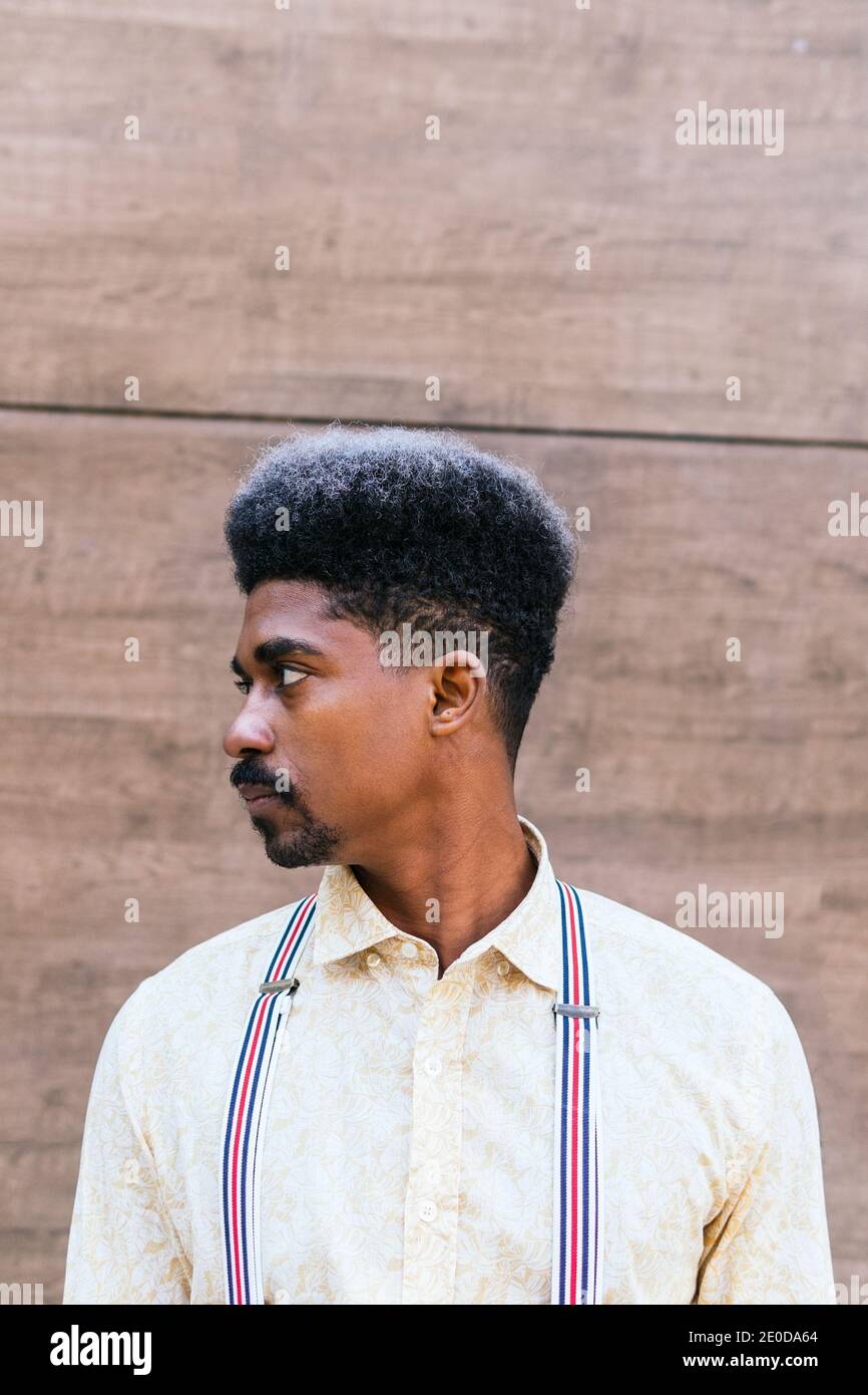 Tranquil serious stylish African American male with curly hair wearing suspenders standing on concrete wall of building and looking away while dreamin Stock Photo - Alamy Tranquil serious stylish African American male with curly hair wearing suspenders standing on concrete wall of building and looking away while dreamin Stock Photo - Alamy