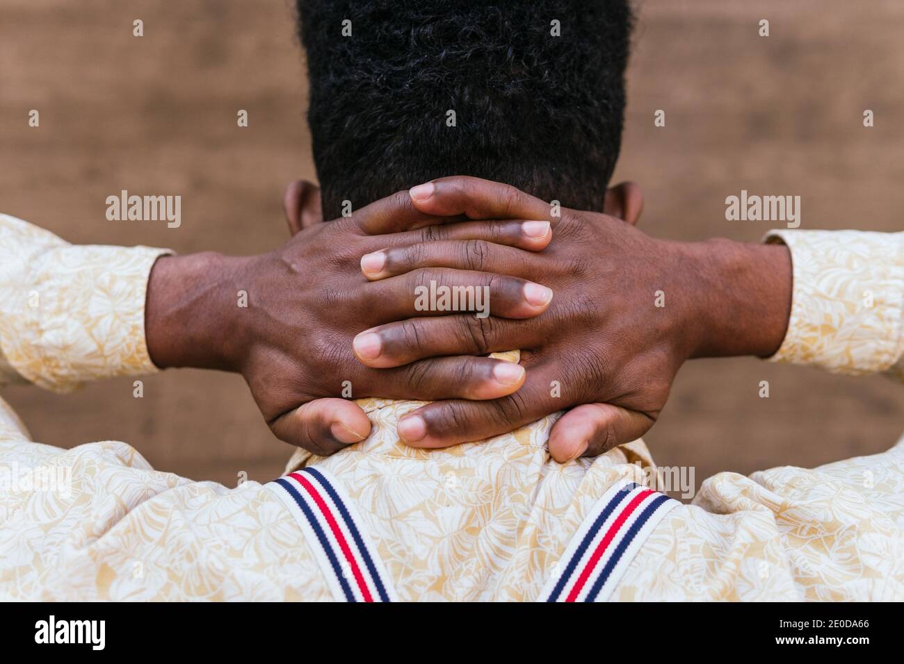 Back view of crop unrecognizable African American male in casual shirt keeping intertwined fingers on neck while relaxing and dreaming Stock Photo