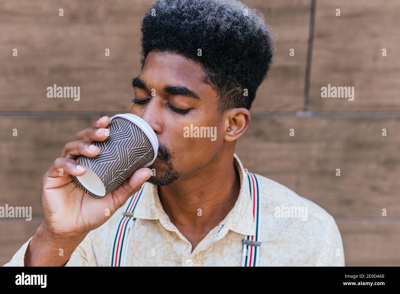 Delighted black male drinking coffee from disposable cup of takeaway with eyes closed Stock Photo