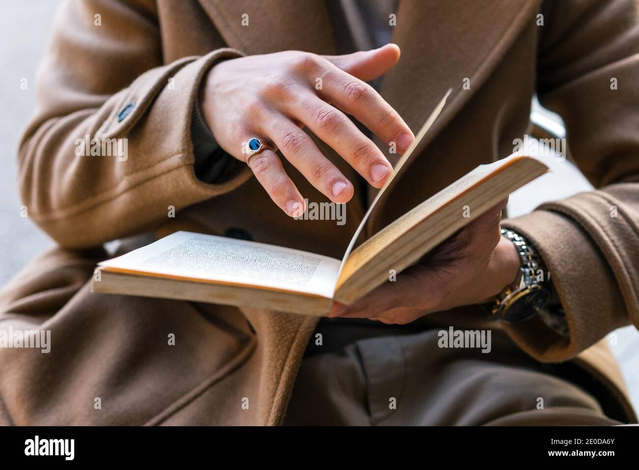 Cropped unrecognizable male in stylish outfit sitting outdoors reading interesting story in book Stock Photo