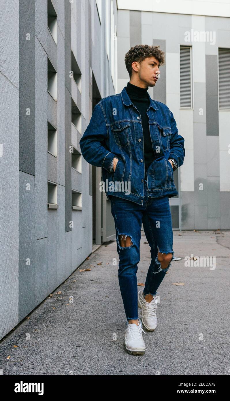 Young determined male wearing denim jacket and jeans standing with hands in  pockets in urban area of city and looking away Stock Photo - Alamy