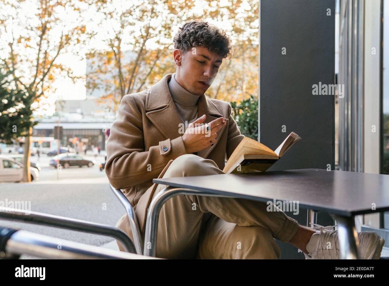 Calm male in trendy clothes sitting on terrace of cafe and reading book