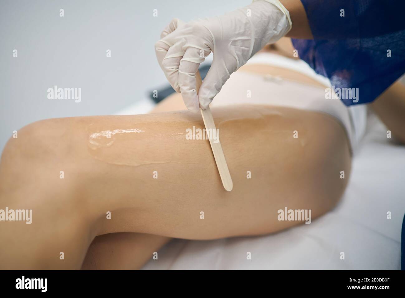 Unrecognizable beautician applying sugar paste with wooden spatula on leg of client while removing hair during skin care procedure in beauty clinic Stock Photo