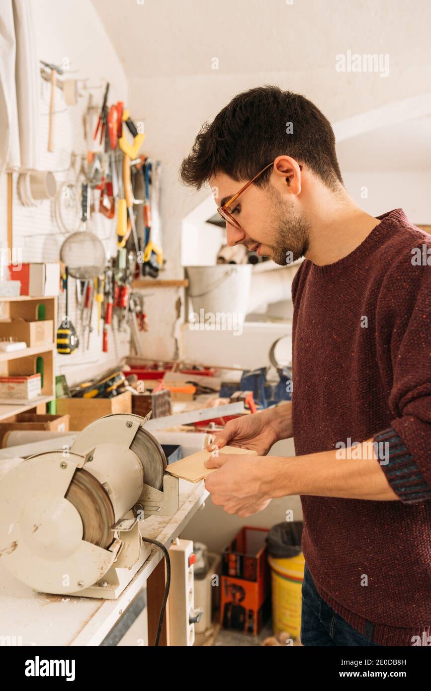 Side view of male carpenter using grinding machine for polishing wooden ...