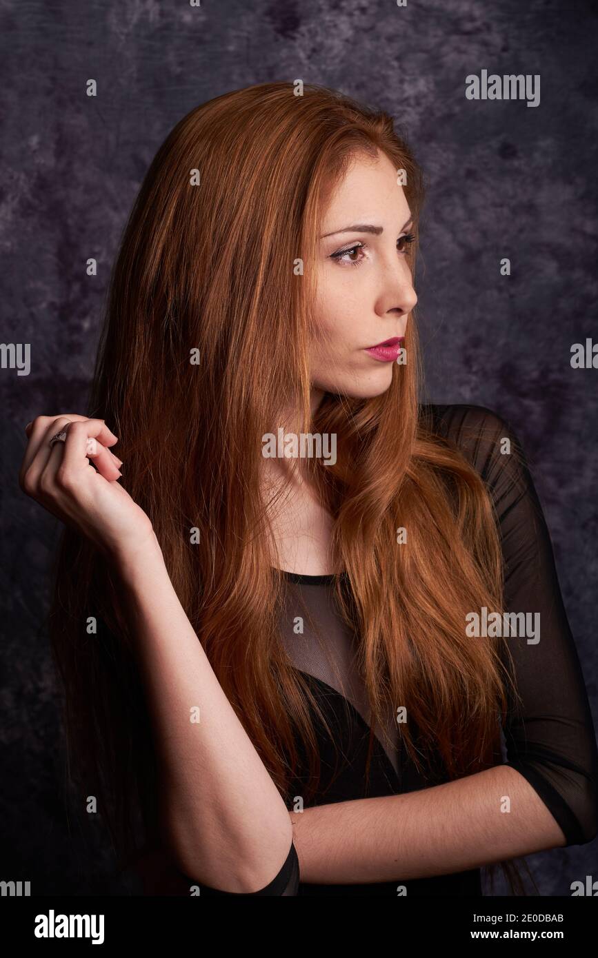 Calm female model in stylish clothes standing in studio with red hair and looking away Stock Photo