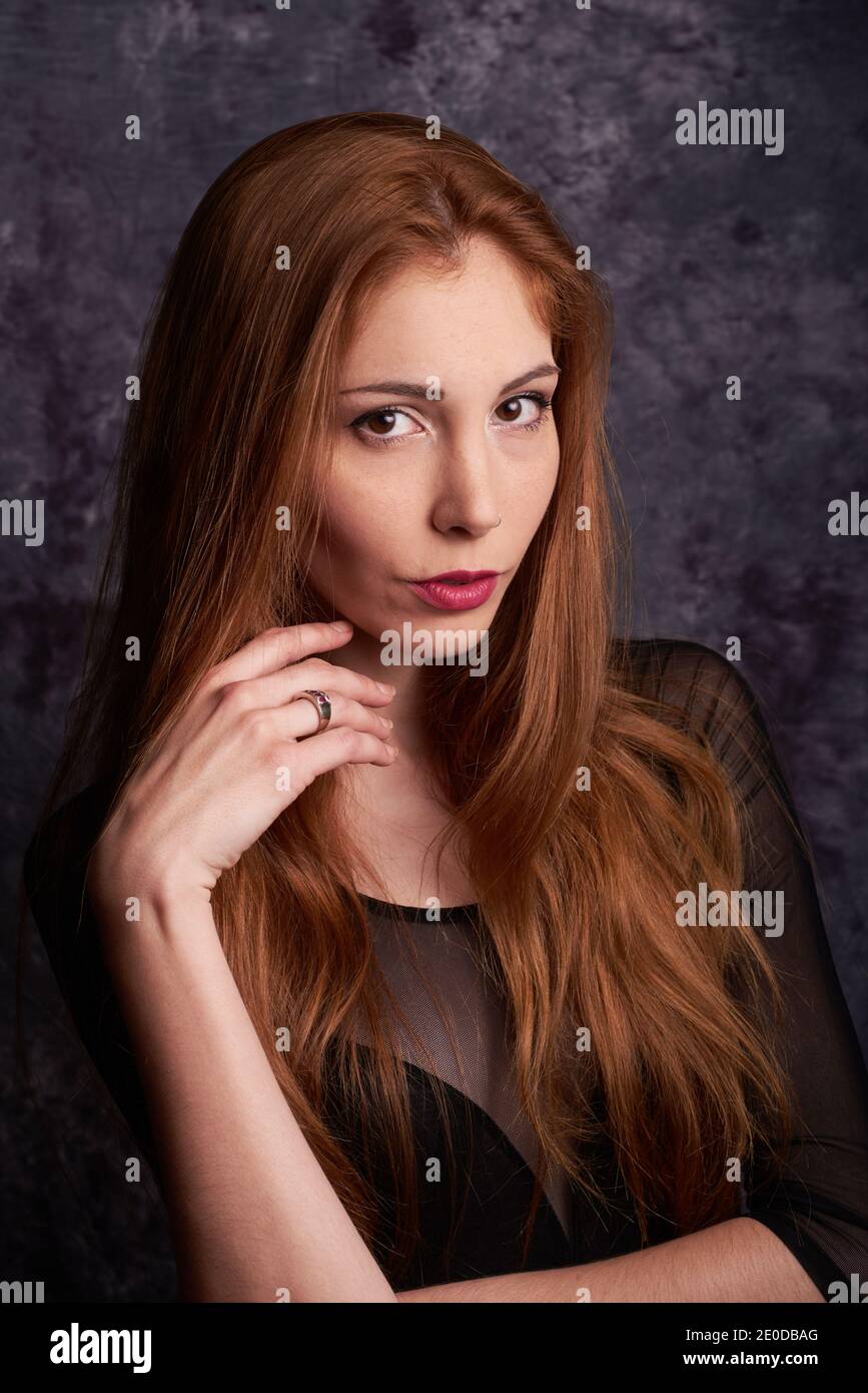 Calm female model in stylish clothes standing in studio with red hair and looking at camera Stock Photo