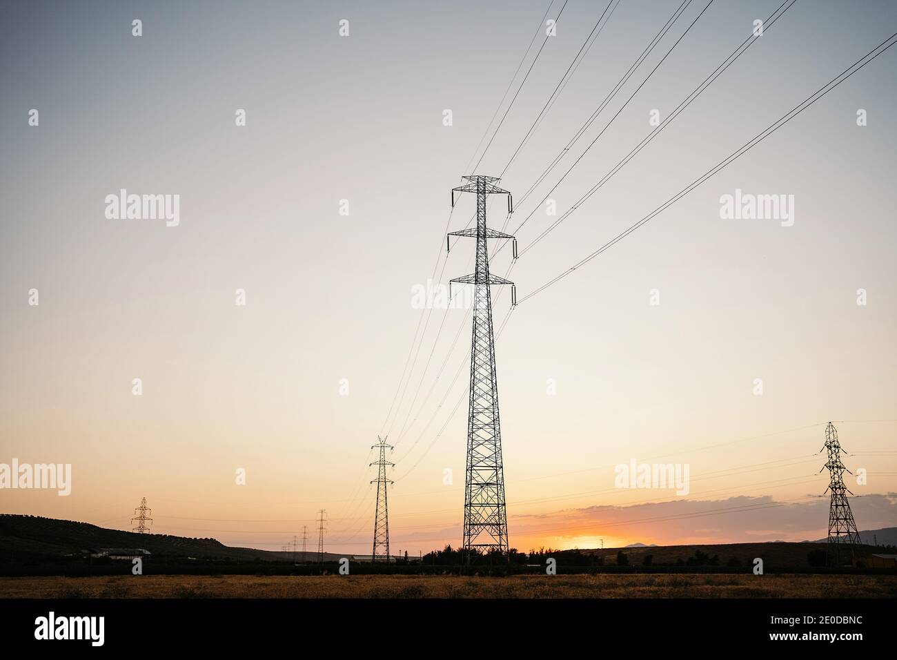 Low angle of tall electricity towers and wires in field under evening ...