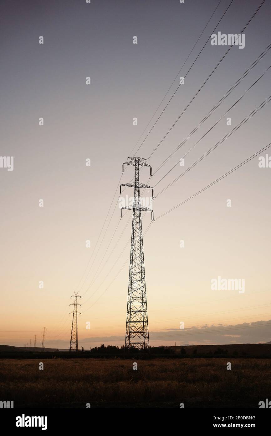 Low angle of tall electricity towers and wires in field under evening ...
