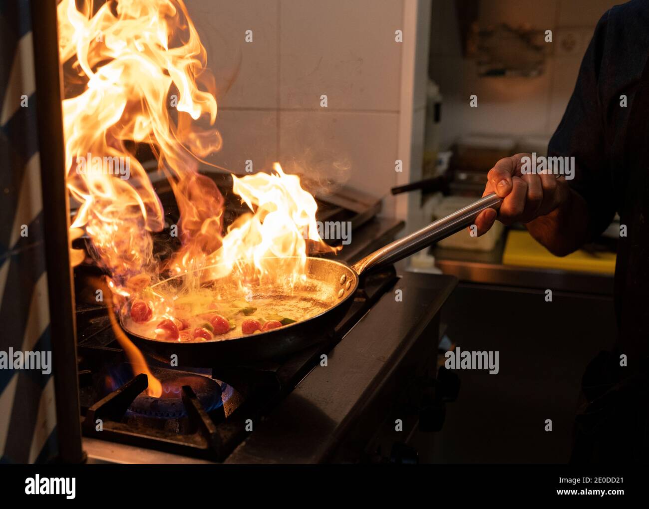 Crop anonymous cook holding frying pan with burning flame while