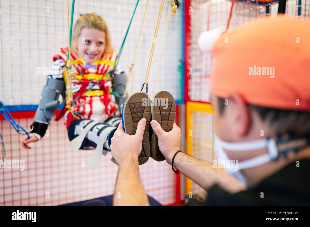 Crop anonymous specialist giving support to girl with Angelman syndrome during rehabilitation training with elastic straps Stock Photo