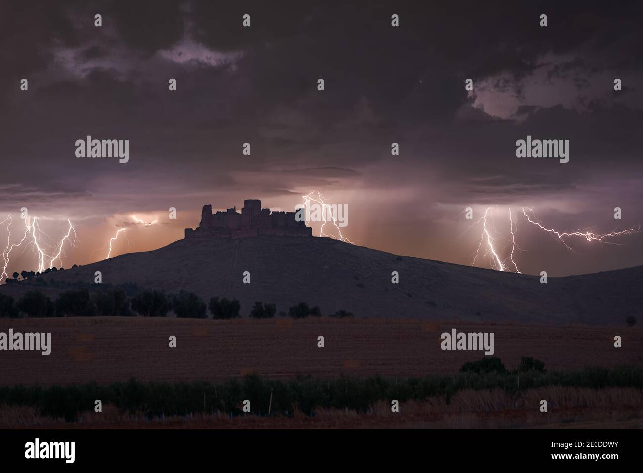 Amazing view of dark thunderstorm sky with bright lightnings striking above stone fortress on hill in  mountains Stock Photo