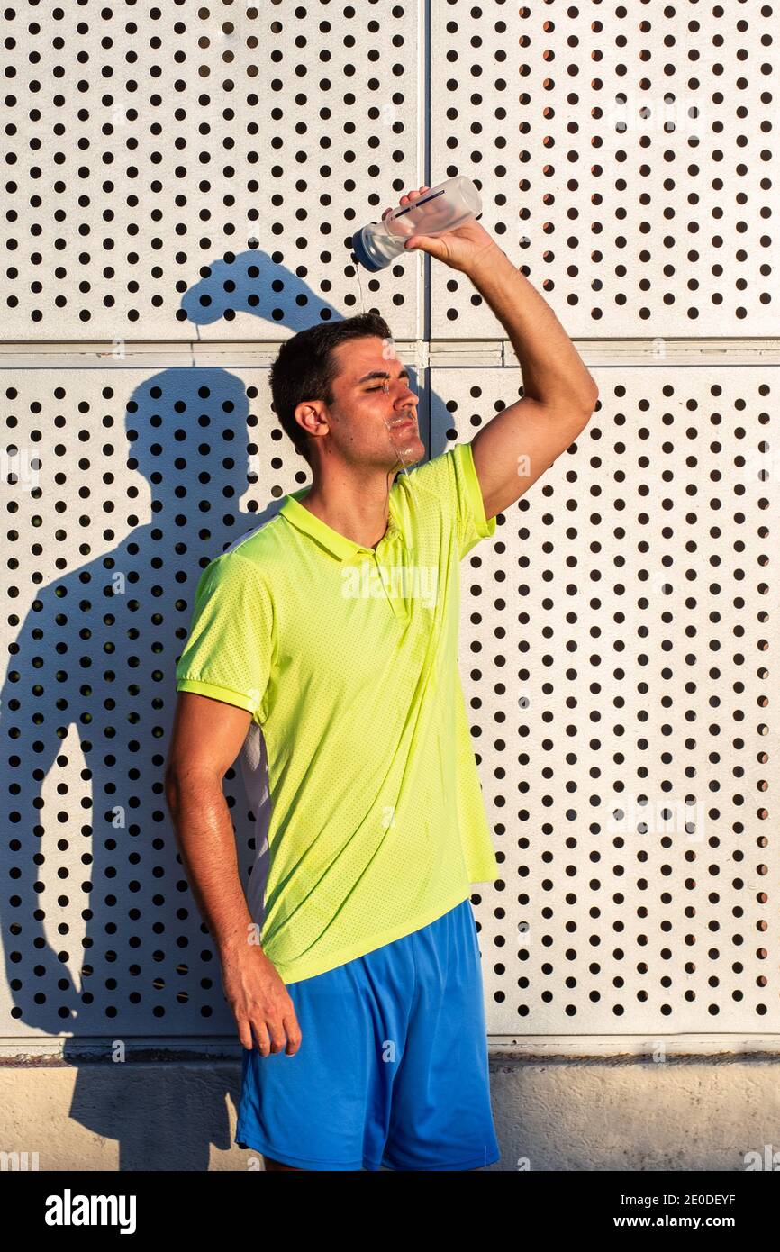Tired male athlete in sportswear pouring cold water from bottle on head