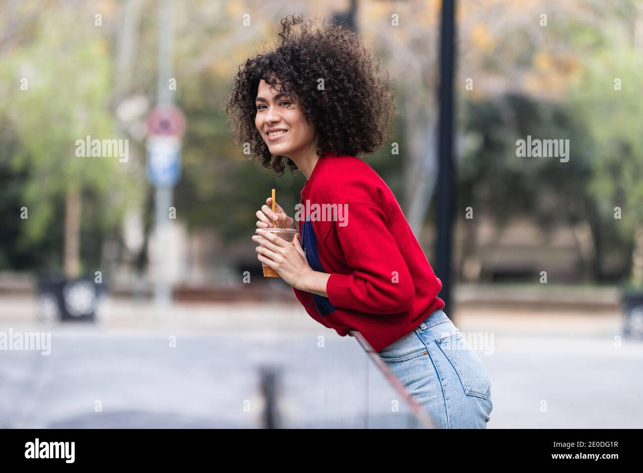 Side view of young African American female standing on street with fresh juice in plastic takeaway cup and enjoying weekend in city Stock Photo