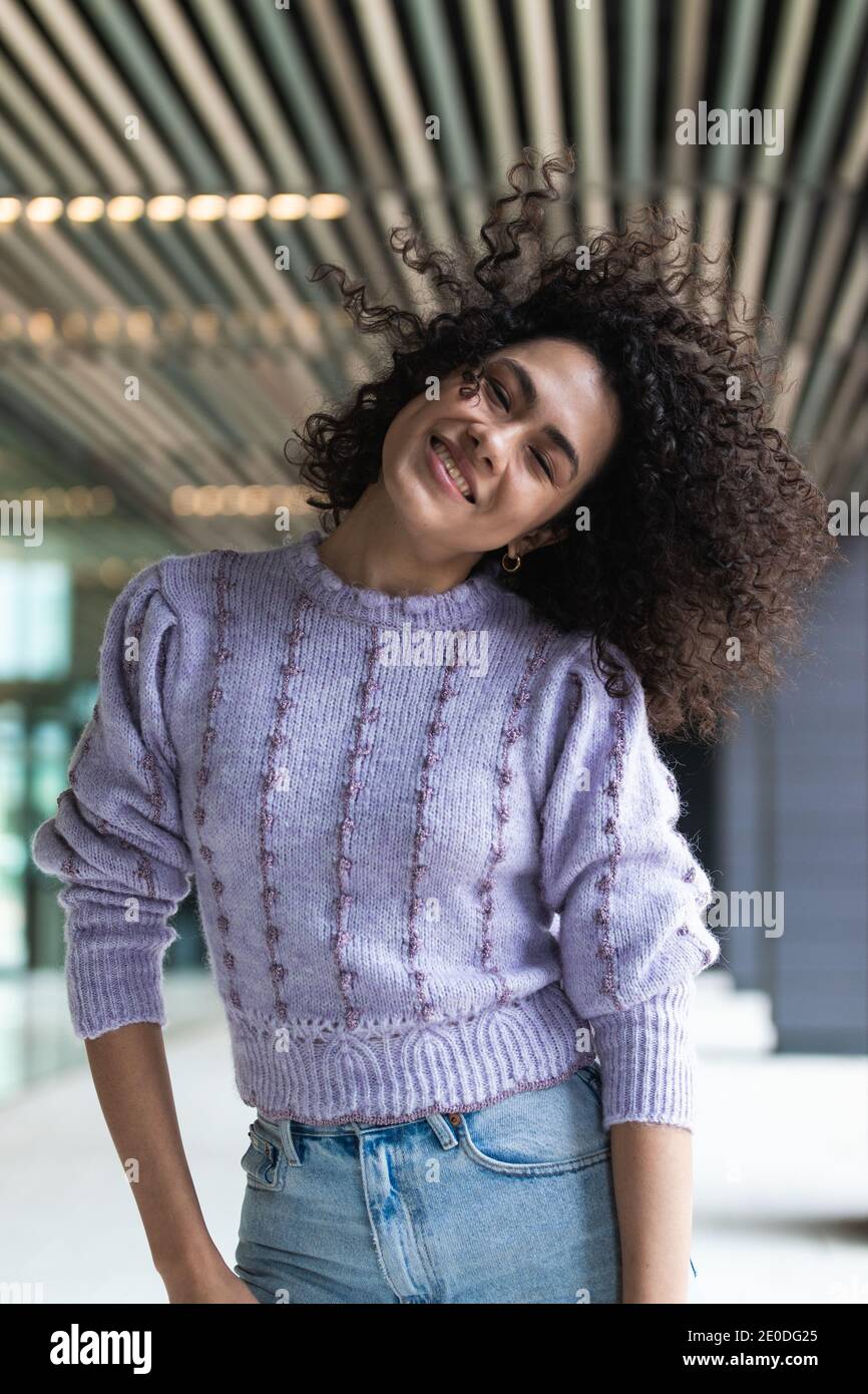 Playful black female with Afro hairstyle standing in street with flipping hair and smiling charmingly at camera Stock Photo