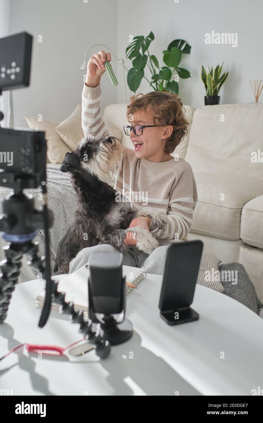 Happy boy playing with his lovely dog and filming a video for his channel. Stock Photo