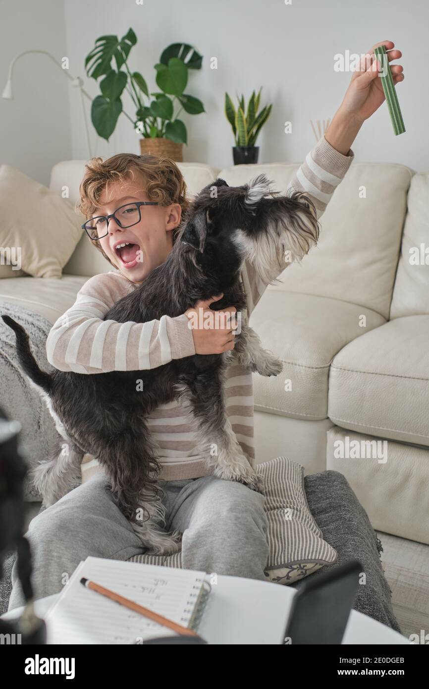 Happy boy playing with his lovely dog and filming a video for his channel. Stock Photo