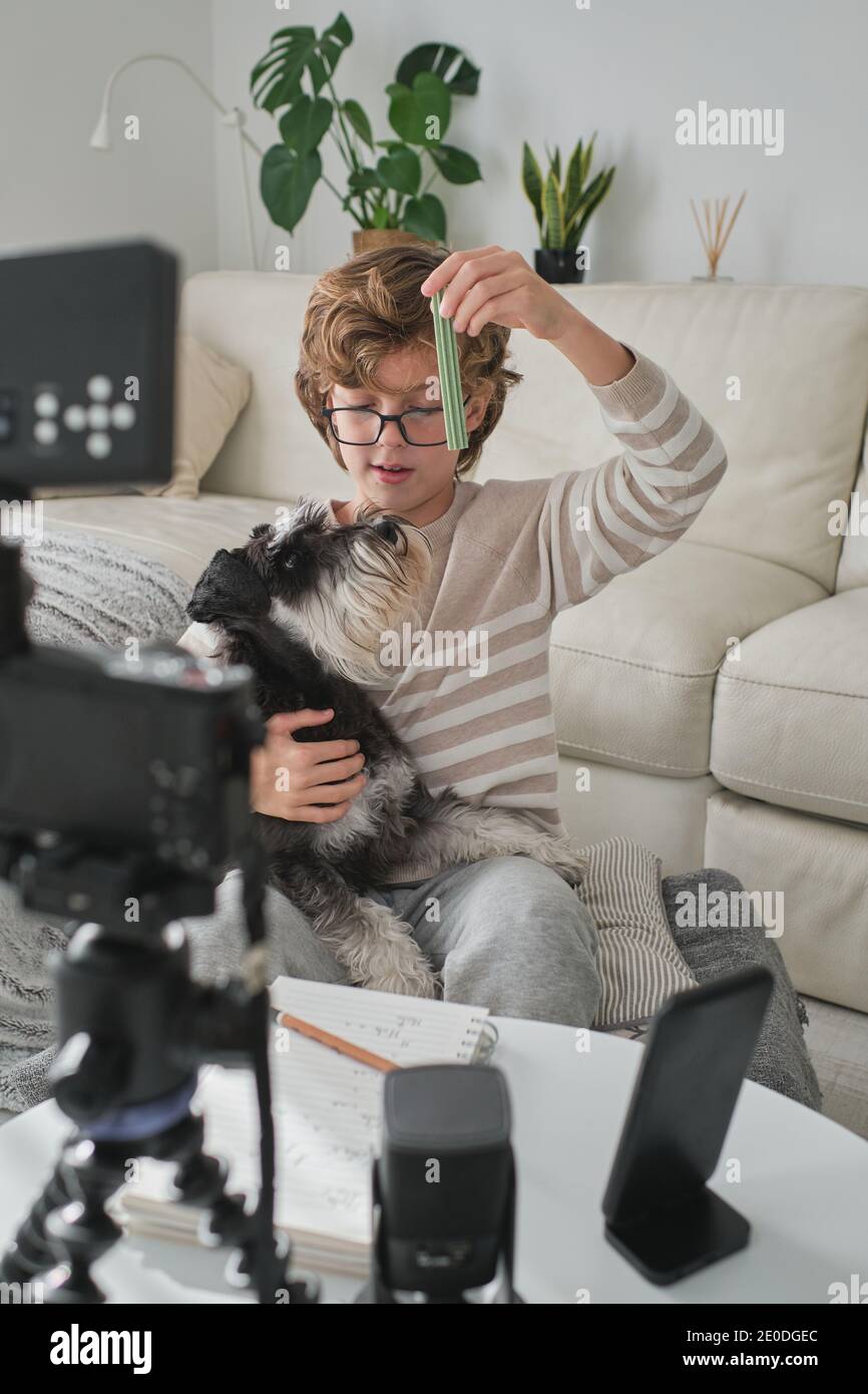 Happy boy feeding his lovely dog and filming a video for his channel. Stock Photo