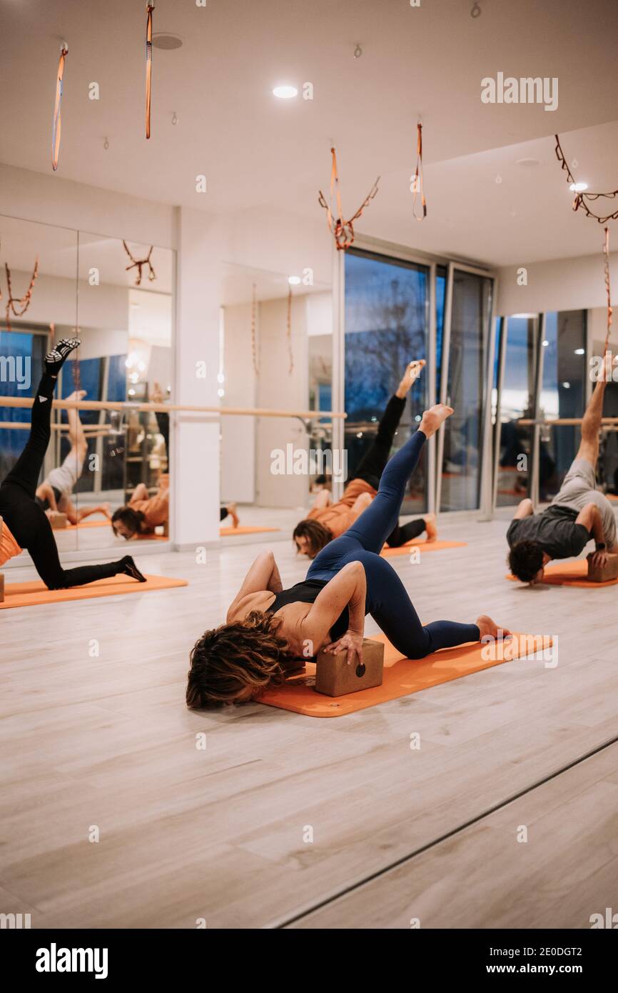 Company of people in sportswear practicing yoga on bricks and mats in Eka Pada Adho Mukha Svanasana in spacious studio in evening Stock Photo