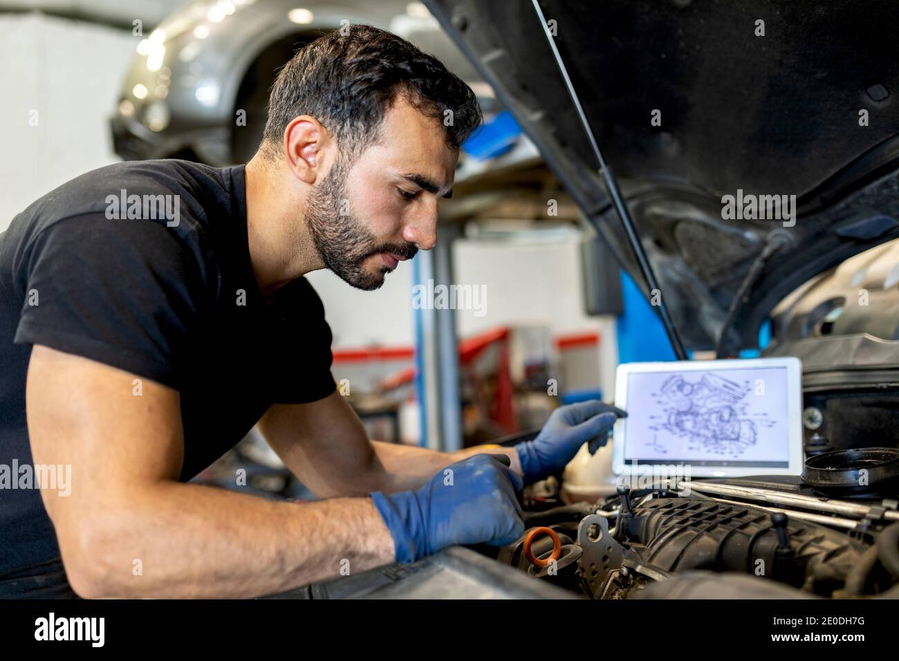 Side view of male technician with scheme of motor on tablet checking car engine during diagnostics in modern service Stock Photo