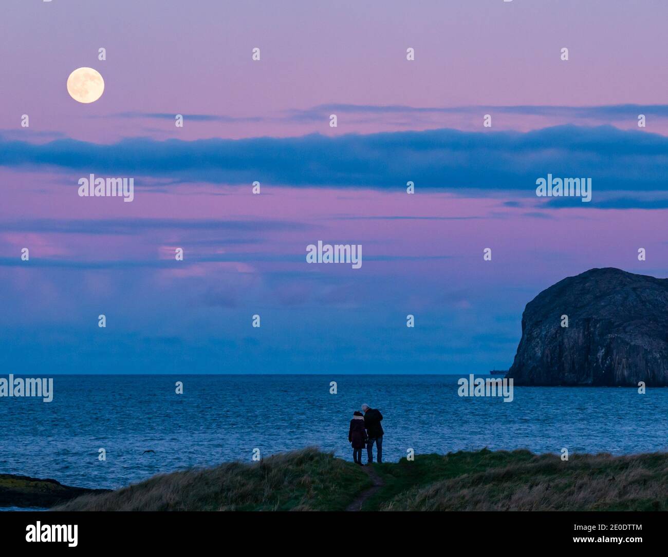 A full moon rises over Bass Rock island with a colourful sunset, Firth of Forth, Scotland, UK Stock Photo