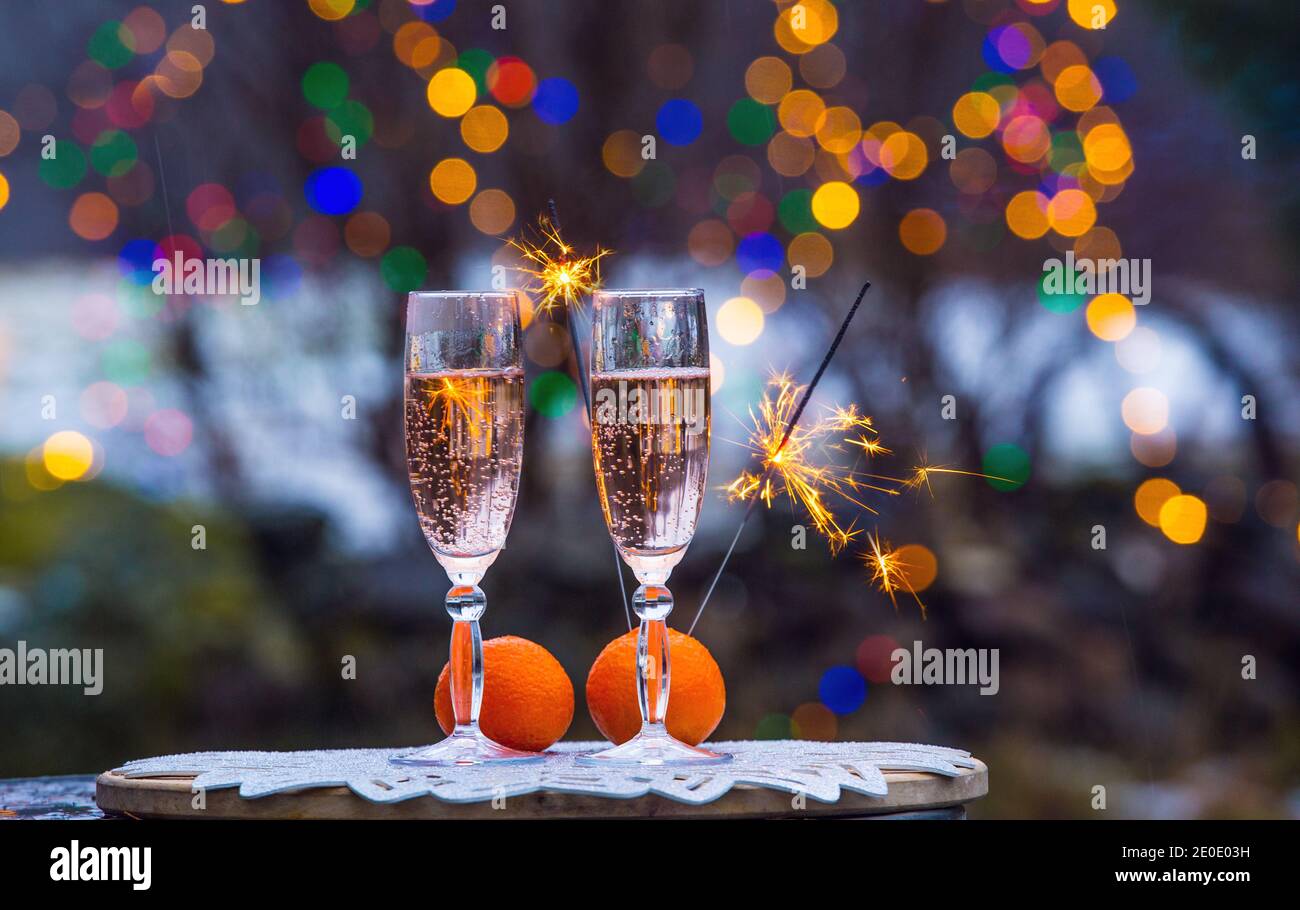 Celebrate New Years eve in home garden outdoors in winter, snowy evening, sparklers sparkle, copy space two flute glasses with champagne. Stock Photo