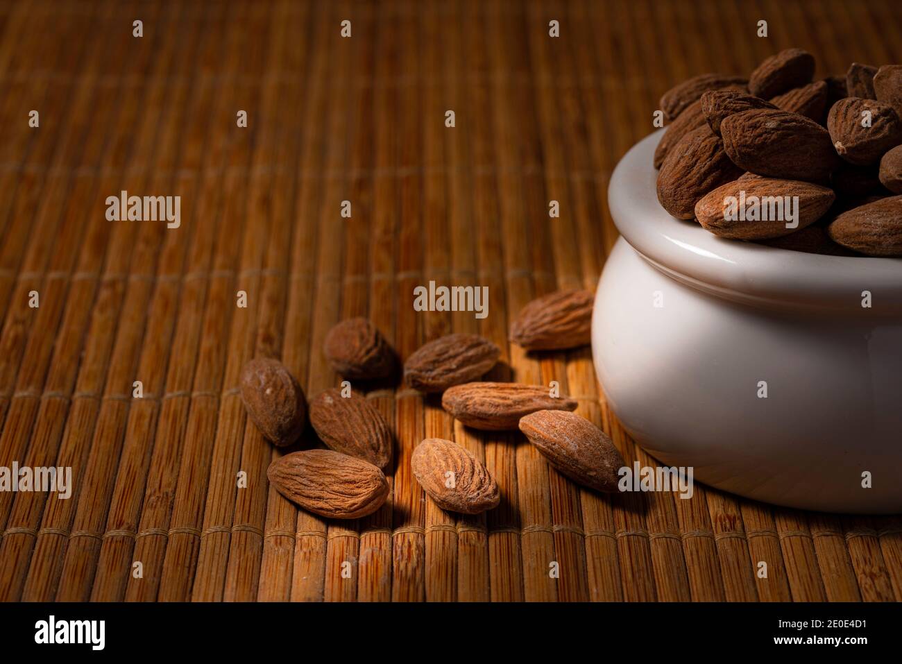 White bowl of salted dry roasted almonds with directional lighting Stock Photo