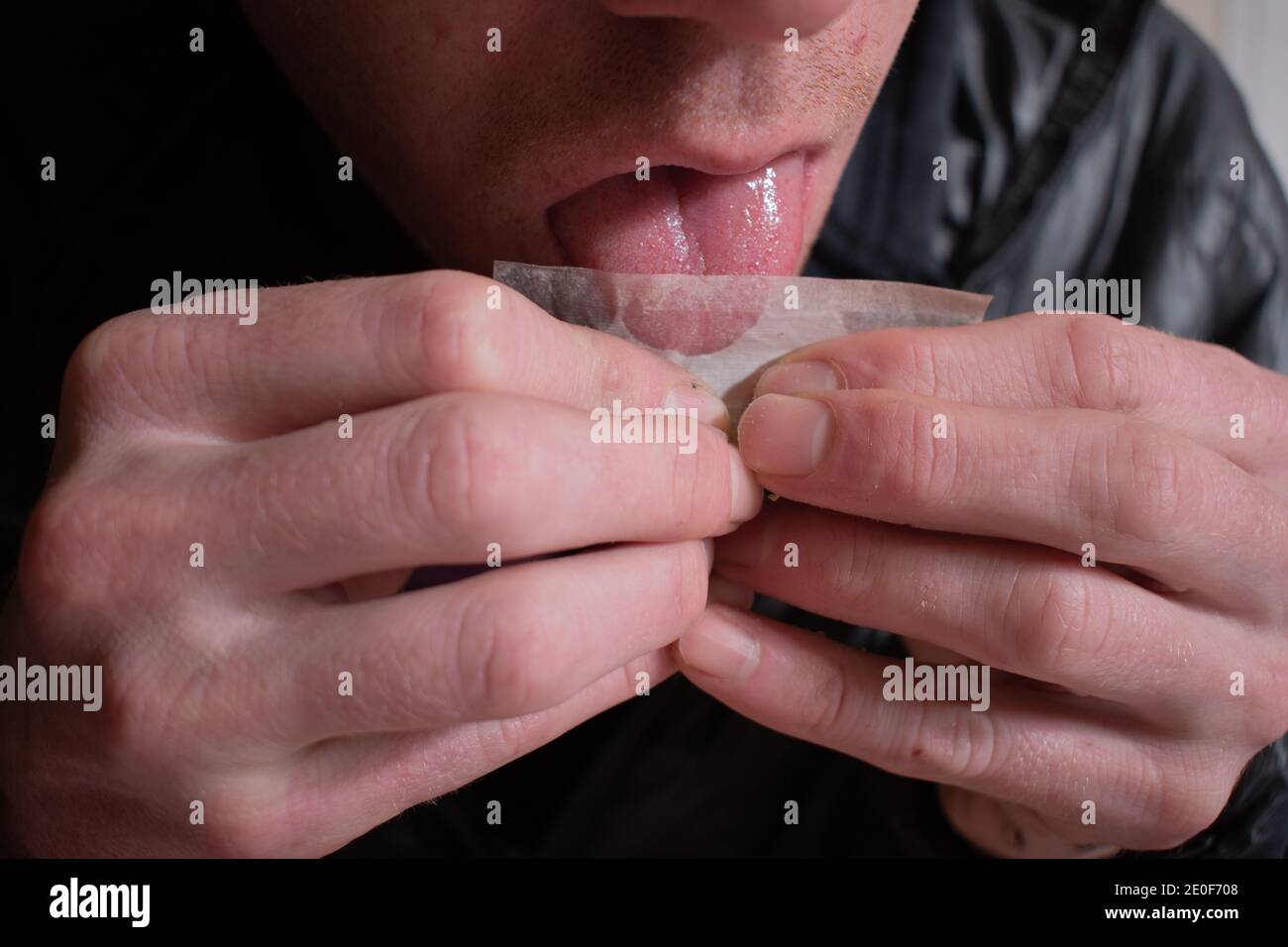 Male licks rolling papers while making a cigarette joint Stock Photo