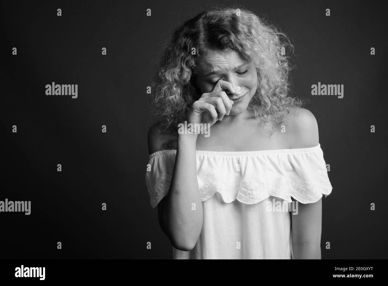 Young beautiful woman with blond curly hair against gray background Stock Photo