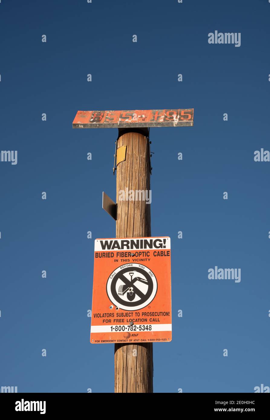 An orange caution sign on a wooden pole warns against digging in that area because of buried cable. Stock Photo