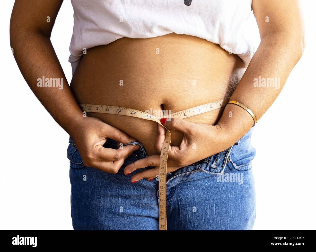 mid section of an Indian woman measuring fat belly with tape on white background Stock Photo