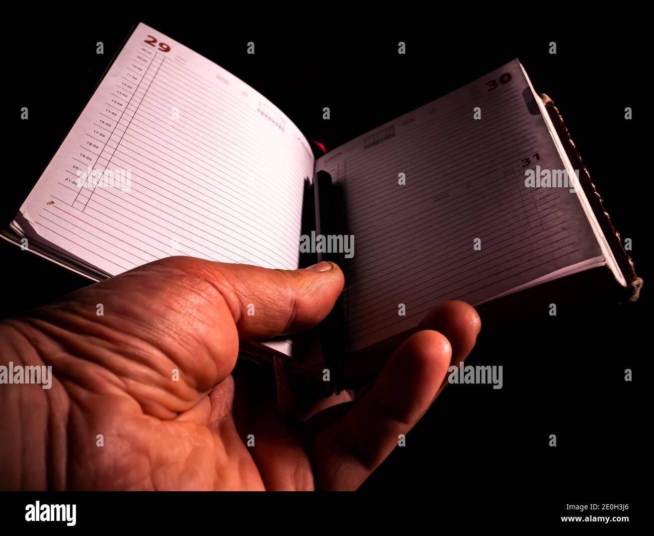 Notebook with a pen in a mans hand on a black background. Notebook for notes. Business weekly. Keep a diary. Business plan. Human hand. Writing pen. B Stock Photo